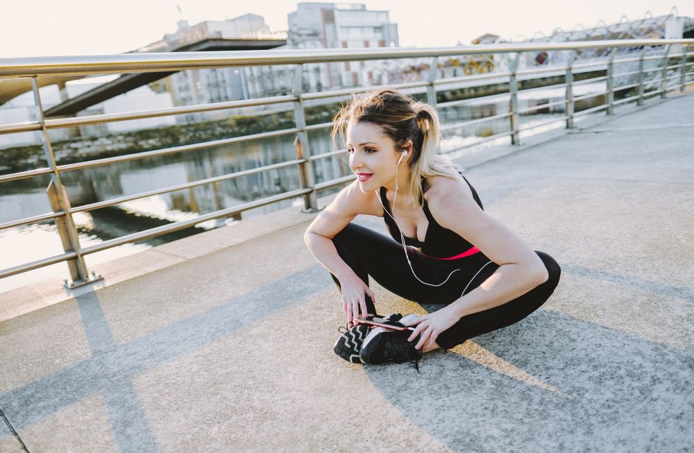 Woman with earphones and smartphone stretching on embankment