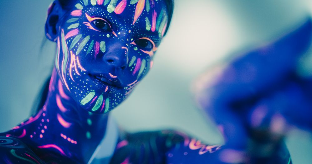 Expressive Female Dancer Transcends Boundaries with Contemporary Dance. Cinematic Portrait of a Young Creative Performer Covered in Neon Body Paint, Looking at Camera, Moving in Improvised Fashion