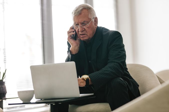Businessman working on laptop and talking on mobile phone in office lobby