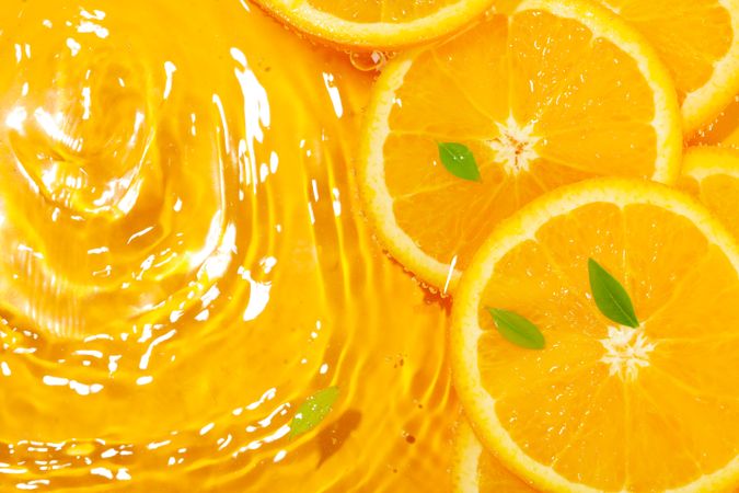 Top view of orange slices with leaves soaking in fresh water with ripples