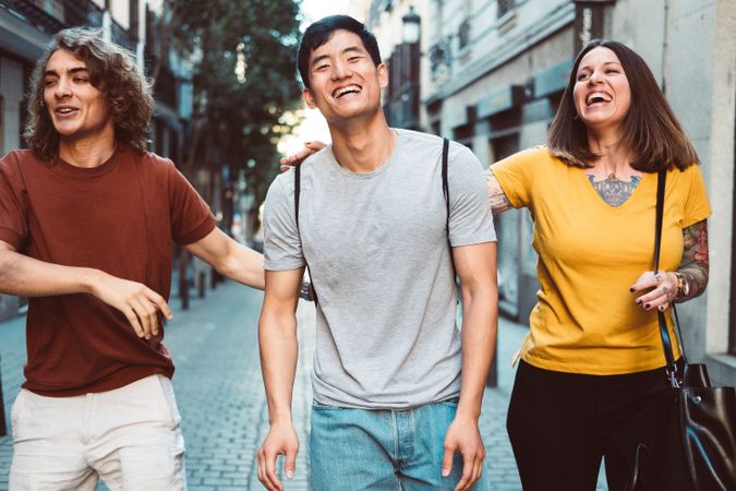 Cheerful multiracial friends hugging and walking along city street