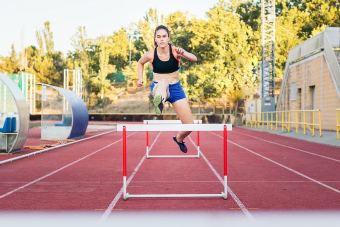 An athletic woman jumping hurdles on an athletics track.
