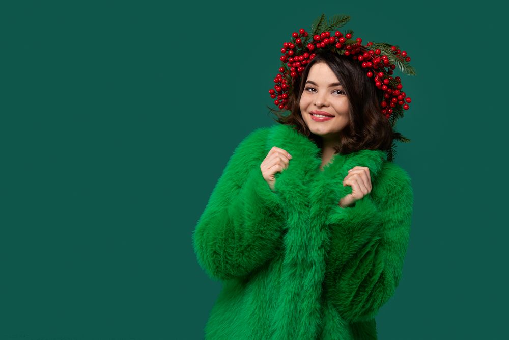 Smiling woman in green coat and red berry wreath posing.
