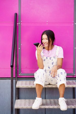 Vertical composition smiling Chinese woman talking on cell phone sitting next to pink