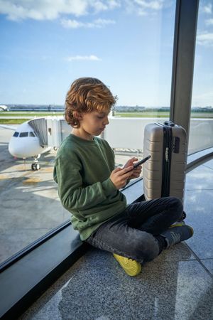 Boy with smartphone near window in airport