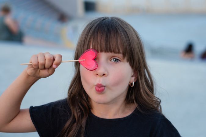 Funny little girl with red heart shaped lollipop