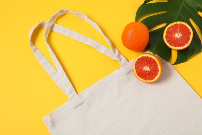 Eco bag, palm leaf and orange on color background, copy space
