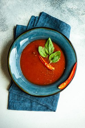 Looking down at traditional Spanish soup of tomato gazpacho with basil garnish in blue bowl