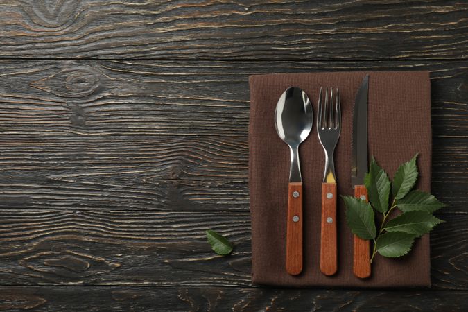 Napkin, fork, spoon, knife and leaf on wooden background