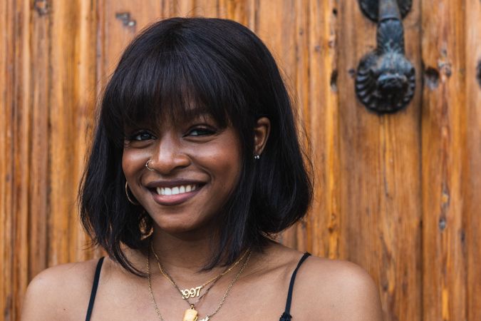 Cheerful Black woman in black outfit against wooden wall