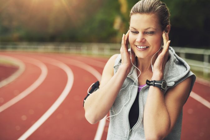 Woman smiling listening to earphones in ear on race track