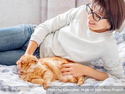 Woman petting fluffy ginger cat pet while laying on the bed bYzjD0