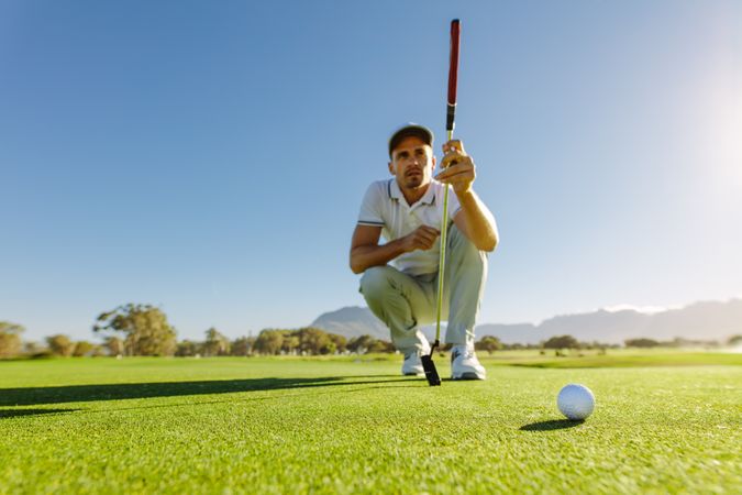 Golfer squatting while analyzing ball