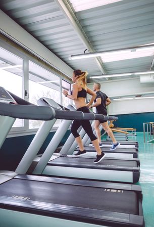 Two people jogging on treadmills in gym