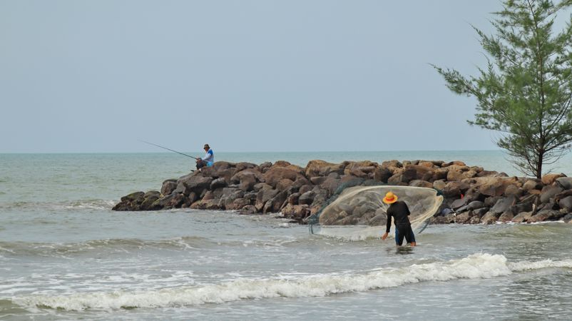 Two men fishing with fishing rod and net on the beach