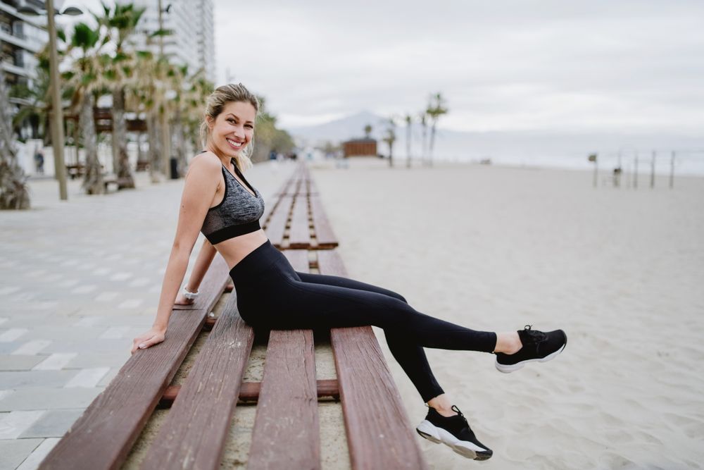Sportswoman resting in a bench at sandy beach