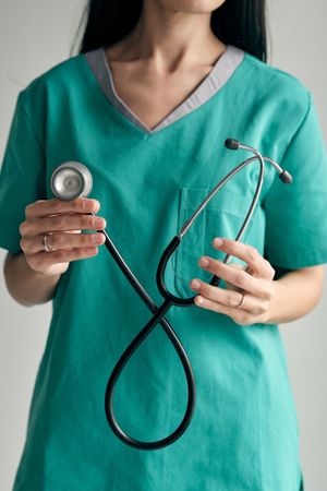 Crop surgeon with stethoscope on light background