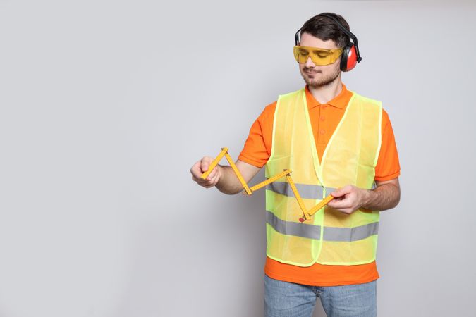 Engineer in headphones with ruler in hands on gray background, space for text