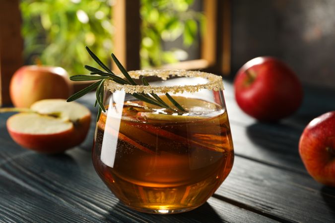 Glass with apple cider and apples on wooden table on light background, close up