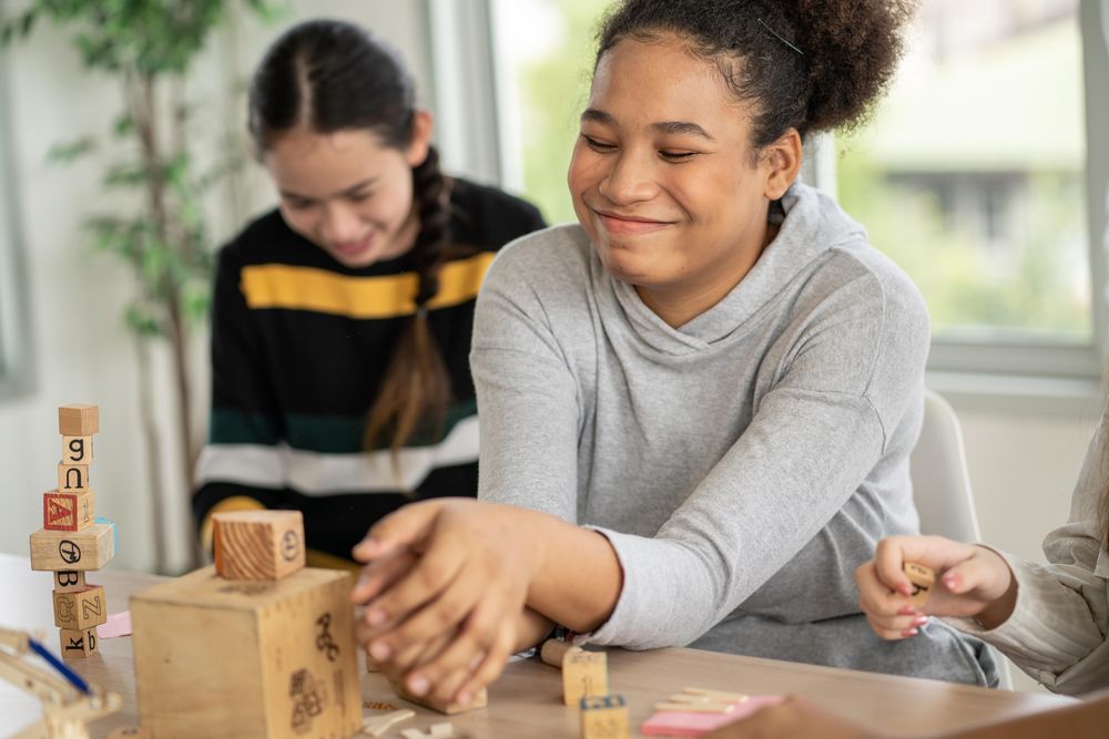Two female students laugh as building blocks fall down