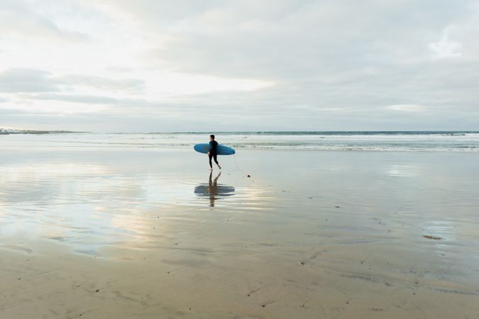 Person with surfboard walking near sea