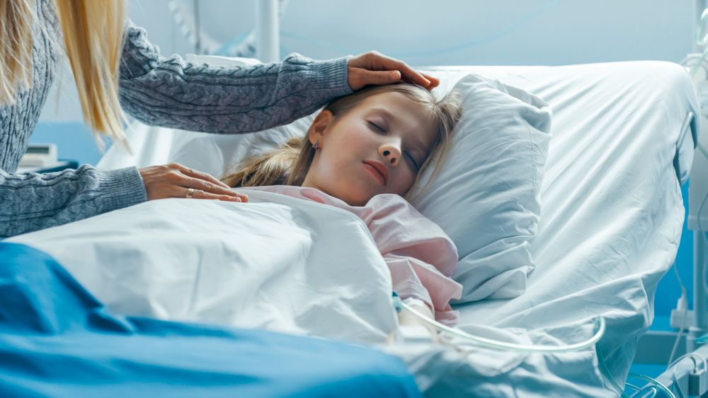 Close-up Cute Little Girl Sleeps on a Bed in the Children's Hospital, Caring Mother Covers Her with a Blanket and Caresses Her Forehead
