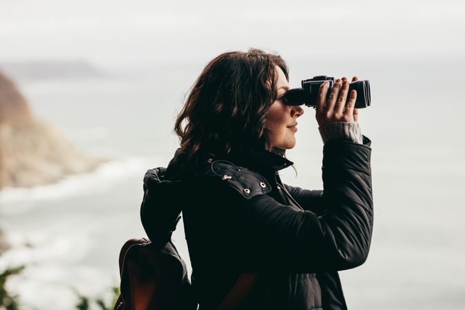 Woman wearing warm jacket looking through binoculars