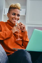 Black woman smiling with a champagne flute looking away from her laptop