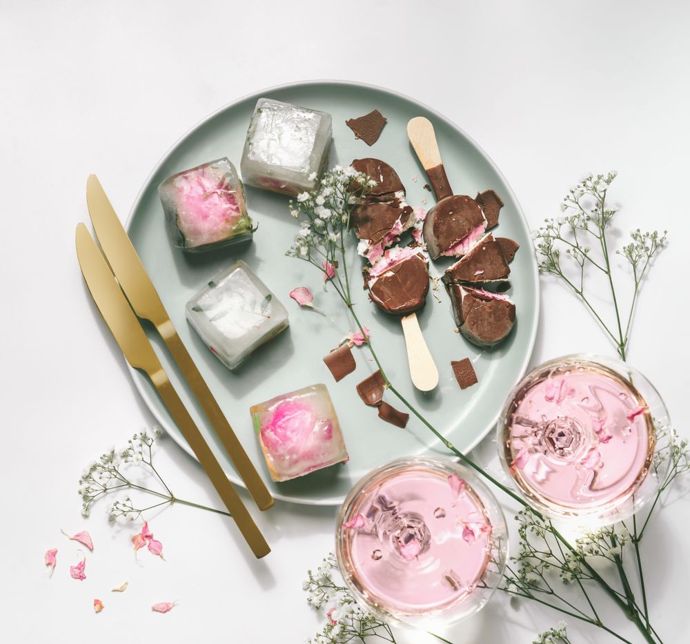 Ice cream popsicles with chocolate on plate with gypsophila,  wine glasses with rose wine, ice cubes and golden knifes