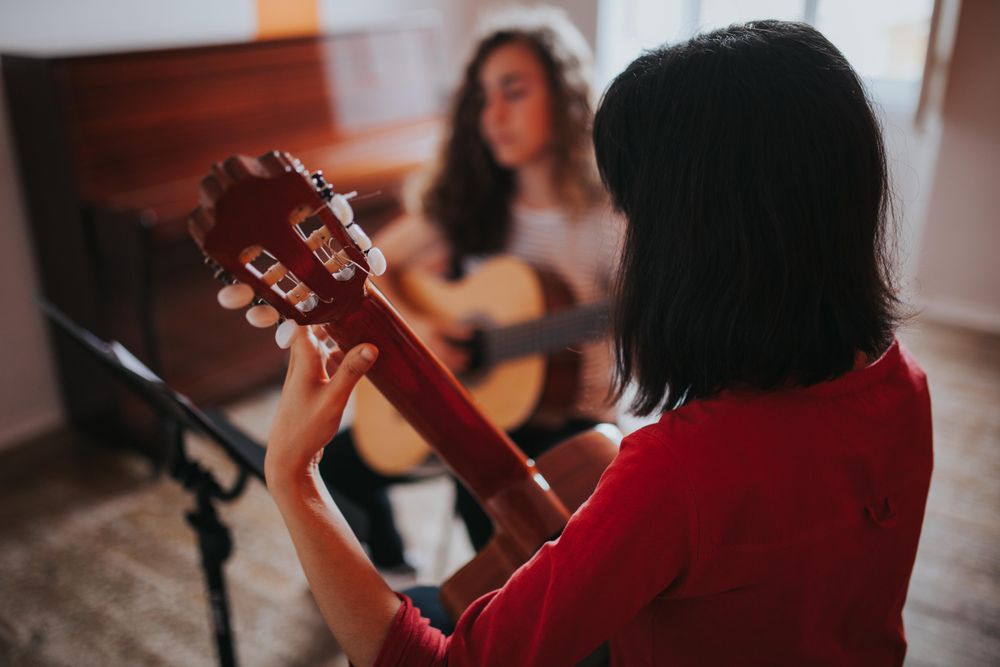 Rear view of young student holding neck of guitar and playing music