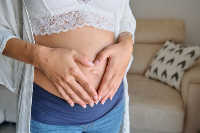Crop pregnant female embracing belly at home