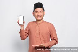 Happy Muslim man in kufi hat presenting mobile phone with black screen bYxZd4
