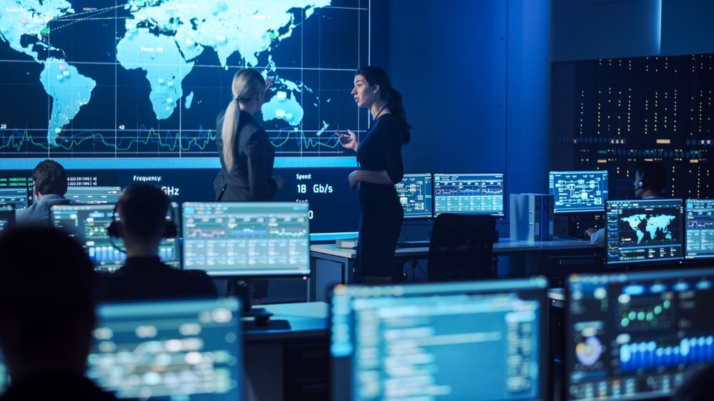 In a Cutting-edge Control Room, Diverse Professionals Engage in Dynamic Discussions, Analyzing Global Data on Multiple Screens to Enhance Cybersecurity Measures and Strategic Operations.