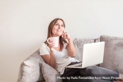Smiling woman on sofa with a cup of coffee working on her laptop in the morning 0J3on5