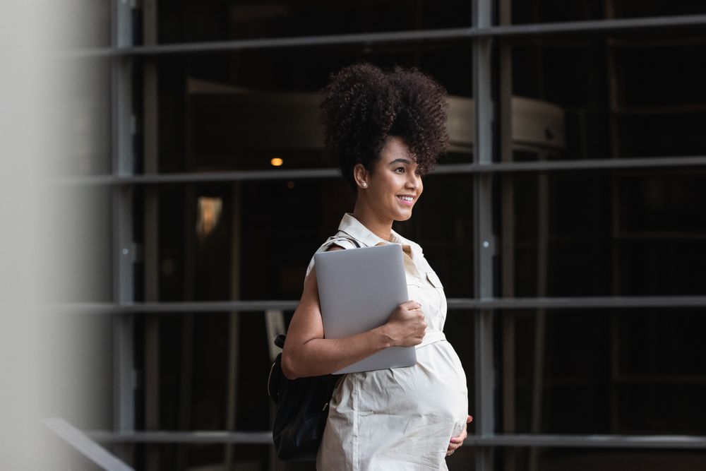 Smiling Black woman with laptop coming out of office building
