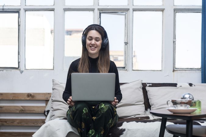 Beautiful Woman wearing headphones sitting on sofa and using laptop
