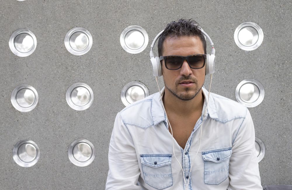 Male listening to music on phone while sitting in front of patterned cement wall