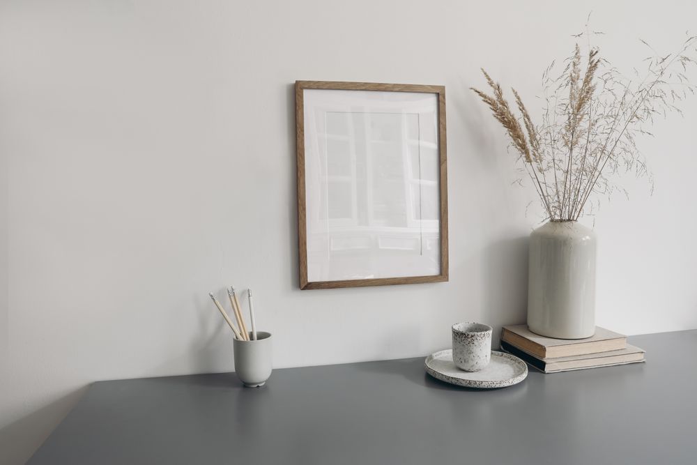Wooden frame hung above desk with vase branches, books and cup of coffee