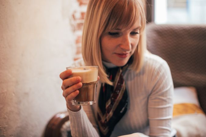 Blonde woman holding latte drink in cafe