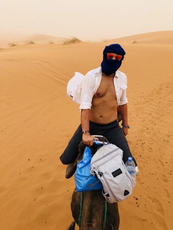 Man wearing shemagh riding a camel in desert