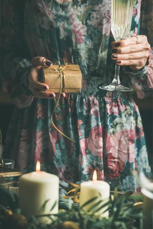 Woman in floral dress with small box with a bow, and flute of champagne, with candles in foreground