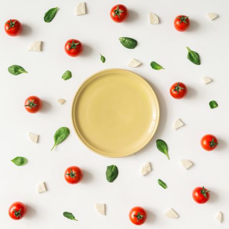 Basil, tomatoes, and cheese on light background with plate