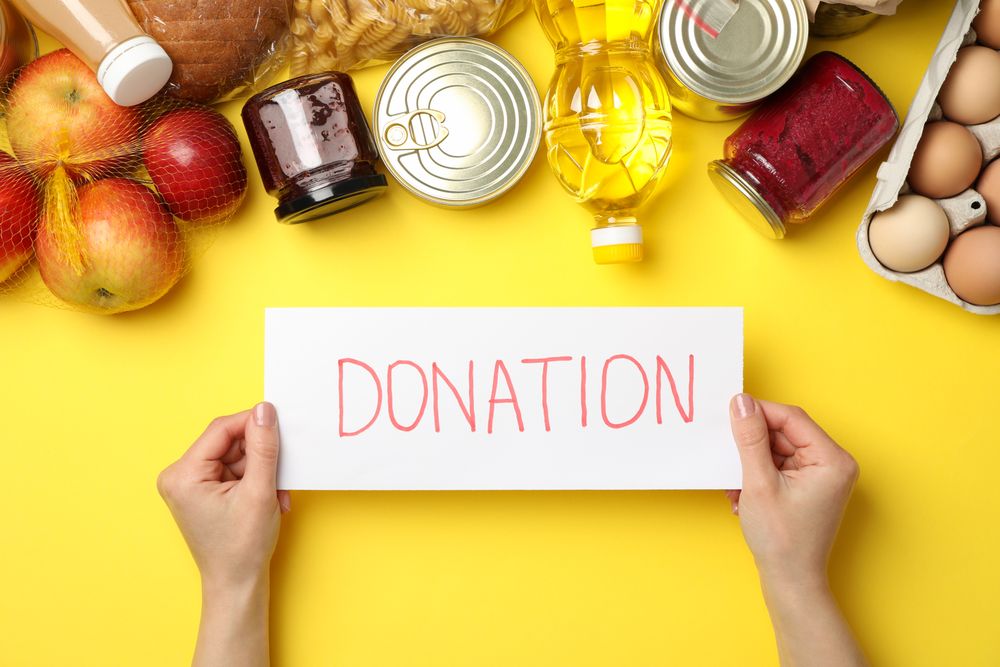 Female hands hold text Donate and different food on yellow background, top view