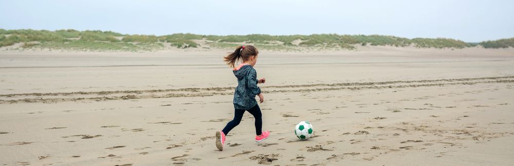 Little girl playing soccer on the beach