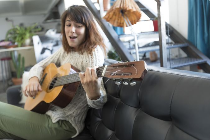 Female on sofa enjoying playing music of her acoustic guitar in living room