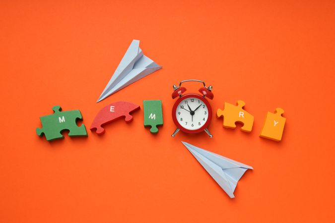 Puzzle pieces spelling “memory” on orange background with alarm clock