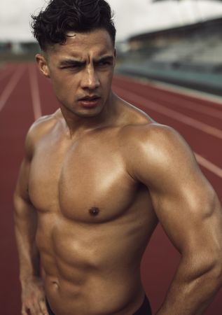 Young man with muscular body standing on a running track and looking away