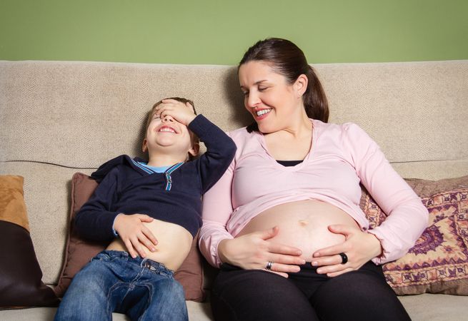 Pregnant mother and son laughing and comparing bellies