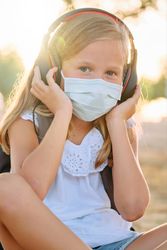 Adorable girl in protective mask and headphones