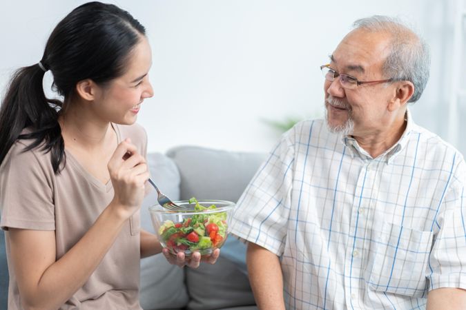 Mature man smiling while eating tasty food from beloved daughter